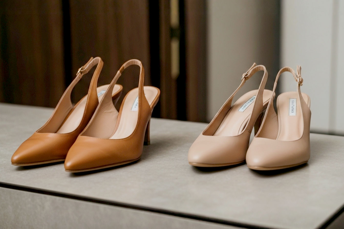 Professional photography style image: A pair of elegant tan leather slingback heels placed next to a pair of elegant light tan matte leather slingback heels on a sophisticated, neutral-toned surface. The background should be slightly blurred, suggesting a stylish wardrobe or dressing area. The lighting should be soft and flattering, highlighting the different warm tones of the slingbacks and the subtle, skin-blending quality of the other shoes The image should convey versatility and classic fashion, suitable for a comprehensive style guide. Lifelike and high-resolution.