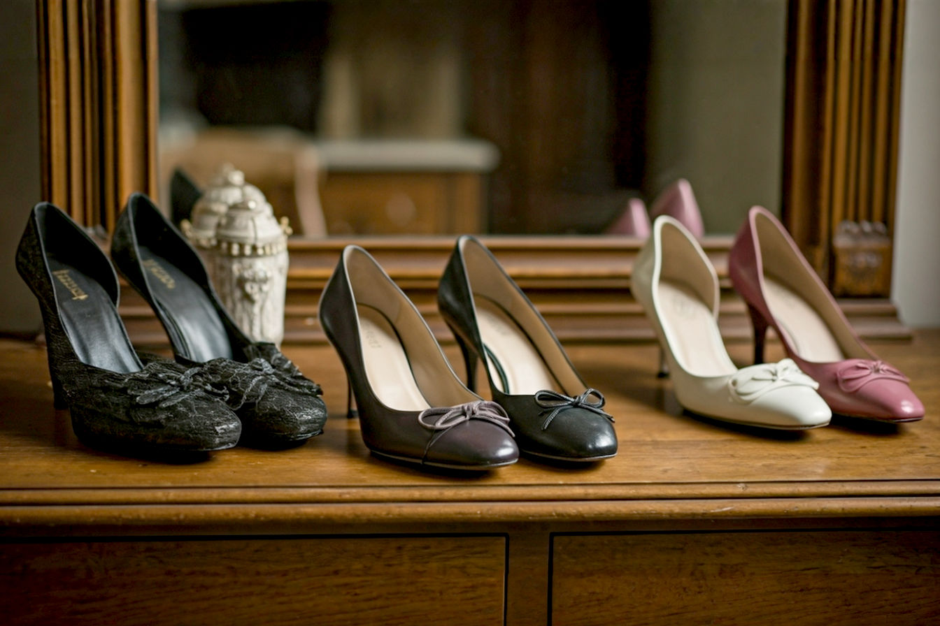 Pro photography style, lifelike, highly detailed shot of a diverse collection of vintage kitten heels from different eras (1950s, 1960s, 1980s, 1990s, 2000s). The shoes are elegantly arranged on a rustic wooden vanity or a velvet-draped surface, perhaps with a soft, diffused light highlighting their varying textures and shapes. Some shoes could be on a shoe tree. Include elements suggesting age and luxury without appearing worn out. The background should be subtly blurred to keep focus on the shoes, evoking a sense of timeless fashion and discovery. Warm, inviting color palette. Natural light.