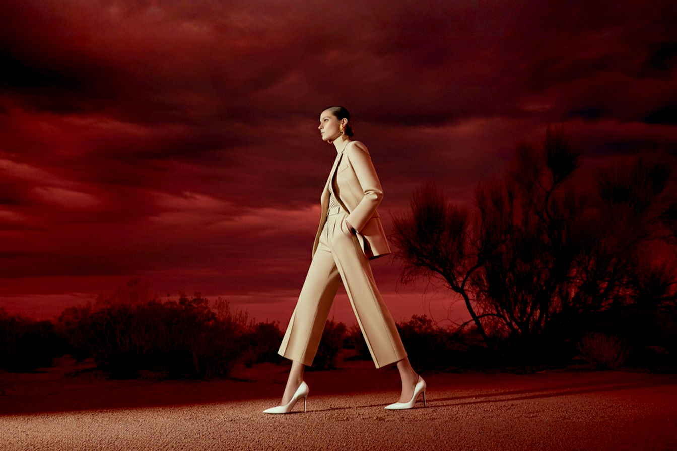 A stylish woman in a chic, seasonally ambiguous outfit (e.g., a tailored blazer and flowy trousers, or a sophisticated midi dress) confidently striding, wearing immaculate white stiletto heels. The background should subtly blend elements of both autumn/winter (e.g., warm earthy tones, bare tree branches in soft focus) and spring/summer (e.g., soft daylight, muted greenery), creating a harmonious, timeless atmosphere. Pro photography style, lifelike, high fashion editorial, soft natural lighting.